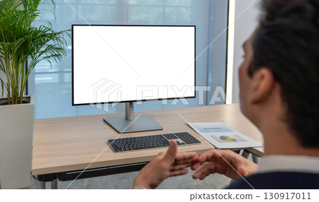Individual is focused on a blank computer screen in a contemporary office environment. A document with a chart is visible on the desk, indicating preparation for a presentation. Individual is focused on a blank computer screen in a contemporary office environment. A document with a chart is visible on the desk, indicating preparation for a presentation. 130917011