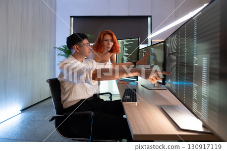 Two colleague engage in a collaborative discussion about data displayed on monitor. One pointing at the screen while the other observe intently. 130917119