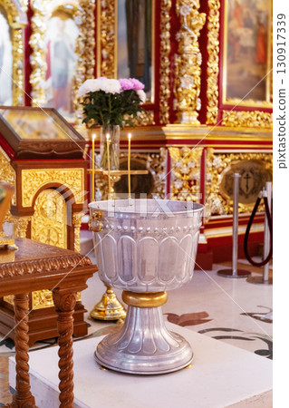 Baptismal font in ornate Christian church interior with candles and icons. Religious symbol of faith, christening tradition, and Orthodox baptism ceremony. Baptismal font in ornate Christian church interior with candles and icons. Religious symbol of faith, christening tradition, and Orthodox baptism ceremony. 130917339
