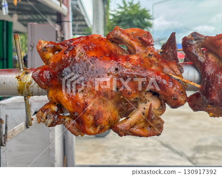 Juicy whole chicken are roasting on a rotisserie over charcoal at a street vendor stall. Close up Juicy whole chicken are roasting on a rotisserie over charcoal at a street vendor stall. Close up 130917392