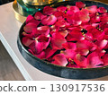 Vibrant rose petal rest on the surface of water in a bowl, creating a calming focal point in a wellness center. Soft light enhances the soothing atmosphere, ideal for meditation. 130917536