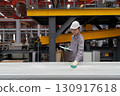 Young asian worker in safety helmet and protective gloves checking material covered in plastic. Work atmosphere in metal sheet manufactory. 130917618