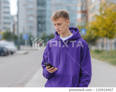 Young man texting on phone in city setting. Stylish vibe for chatting or online themes, great for social or lifestyle ideas. Perfect for digital or urban visuals. 130918407