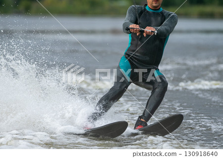 man in full wetsuit riding water skis on lake 130918640