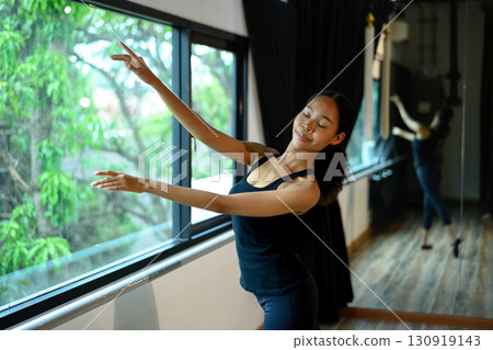 Ballet student performing a delicate pose near the studio window 130919143