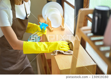 Young woman smiling while cleaning kitchen shelves with spray bottle and cloth Young woman smiling while cleaning kitchen shelves with spray bottle and cloth 130919160