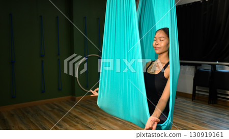 Young woman meditating inside an aerial yoga hammock in a peaceful studio. Young woman meditating inside an aerial yoga hammock in a peaceful studio. 130919161
