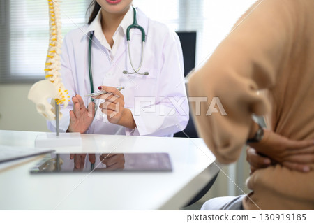 Patient holding lower back while doctor provides advice with anatomical spine model Patient holding lower back while doctor provides advice with anatomical spine model 130919185