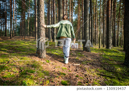 Back view of woman walking through forest between pine trees and foraging for mushrooms in autumn 130919437