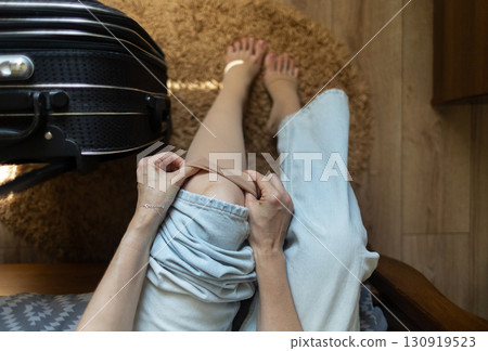 Woman putting on compression stockings before a long trip, suitcase in the background. Concept of leg protection during travel, varicose veins and deep vein thrombosis on long flights or car journeys Woman putting on compression stockings before a long trip, suitcase in the background. Concept of leg protection during travel, varicose veins and deep vein thrombosis on long flights or car journeys 130919523