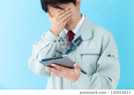 A middle-aged male businessman in work clothes looking at a tablet and worrying 130919813