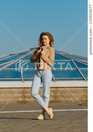 Young woman enjoys a sunny day in casual fashion near a modern glass structure Young woman enjoys a sunny day in casual fashion near a modern glass structure 130920077