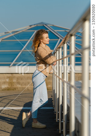 Young woman gazing at the sea while leaning on a railing by the waterfront in bright sunlight Young woman gazing at the sea while leaning on a railing by the waterfront in bright sunlight 130920080