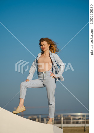 Young woman poses confidently outdoors against a clear blue sky during daylight hours 130920089