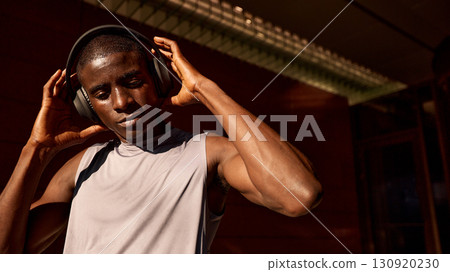 Athletic man enjoying music outdoors wearing headphones during a sunny day Athletic man enjoying music outdoors wearing headphones during a sunny day 130920230