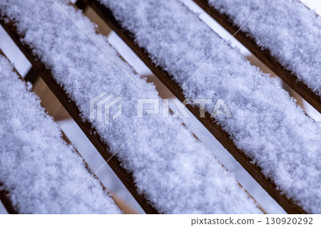Textured parallel wooden slats of an outdoor garden bench covered in a fresh layer of soft white snow, illustrating the serene winter season 130920292