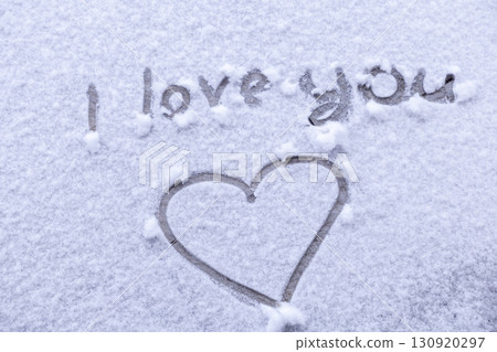 A handwritten I love you message with a heart shape is delicately etched onto a blanket of pristine white snow, capturing tender romantic emotion and winter affection 130920297