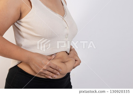 Overweight woman hand pinching excessive belly fat on gray background, Healthy concept 130920335