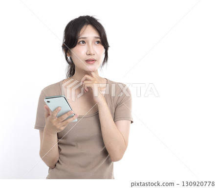 Young woman holding mobile phone and having doubts with confuse face expression 130920778