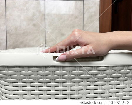 Woman hand opening laundry basket in bathroom. Household chores, laundry routine, home hygiene and cleanliness concept Woman hand opening laundry basket in bathroom. Household chores, laundry routine, home hygiene and cleanliness concept 130921220