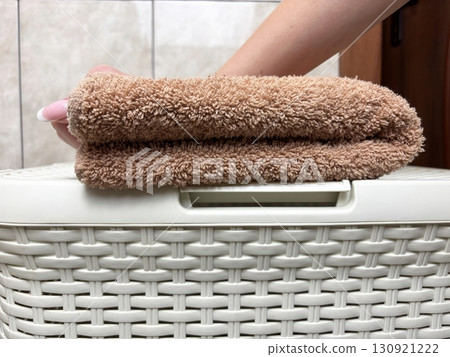 Woman hand folding towel on laundry basket in bathroom. Household chores, washing and towel care concept Woman hand folding towel on laundry basket in bathroom. Household chores, washing and towel care concept 130921222