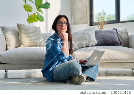 Portrait of young serious woman with laptop sitting at home Portrait of young serious woman with laptop sitting at home 130921436