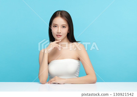 A beautiful young Asian woman with clean, fresh skin against a blue background. Skincare, facial treatment, cosmetology, beauty, and spa. An elegant portrait of an Asian woman. 130921542
