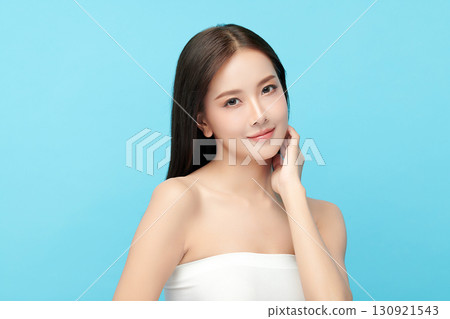 A beautiful young Asian woman with clean, fresh skin against a blue background. Skincare, facial treatment, cosmetology, beauty, and spa. An elegant portrait of an Asian woman. 130921543