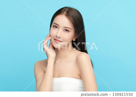 A beautiful young Asian woman with clean, fresh skin against a blue background. Skincare, facial treatment, cosmetology, beauty, and spa. An elegant portrait of an Asian woman. 130921550