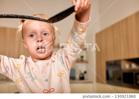 Young girl holding kitchen utensil while standing in a domestic kitchen Young girl holding kitchen utensil while standing in a domestic kitchen 130921860