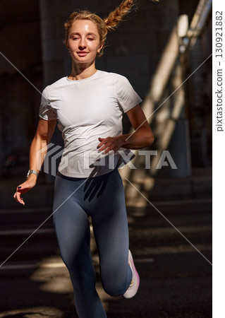 Young woman jogging outdoors in sunlight with energetic and focused expression Young woman jogging outdoors in sunlight with energetic and focused expression 130921882