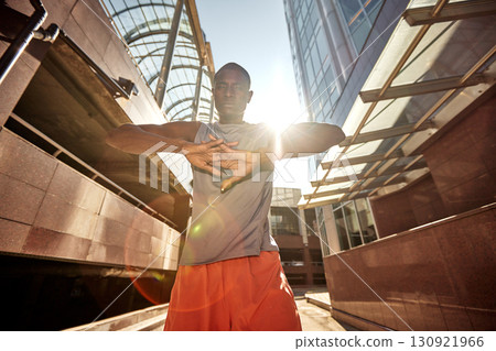 Urban athlete stretching in sunlight near modern buildings 130921966