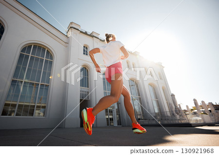 Woman jogging outdoors next to a large modern building in bright sunlight 130921968