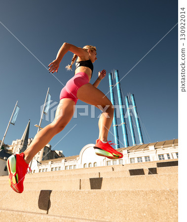 Athletic woman running up stairs under a sunny blue sky Athletic woman running up stairs under a sunny blue sky 130922014