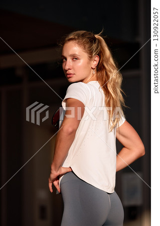 Fit young woman posing confidently in sportswear with natural lighting outdoors Fit young woman posing confidently in sportswear with natural lighting outdoors 130922057