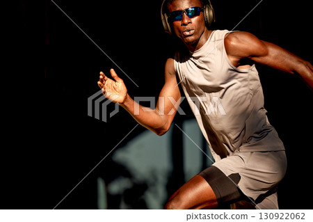 Fit athlete wearing headphones sprinting outdoors under golden hour lighting Fit athlete wearing headphones sprinting outdoors under golden hour lighting 130922062