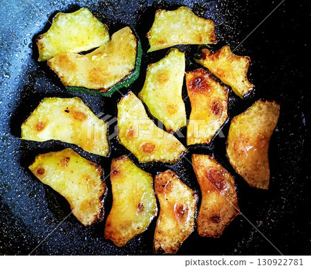 Crispy golden fried zucchini slices cooking in a black frying pan with oil, vegetarian snack food Crispy golden fried zucchini slices cooking in a black frying pan with oil, vegetarian snack food 130922781