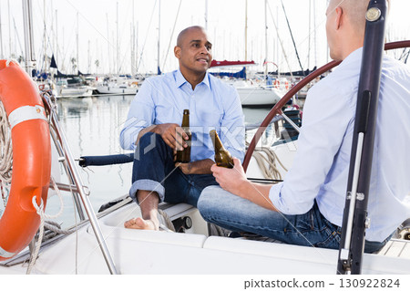 A couple of guys in blue shirts and jeans chatting on a private yacht in the port 130922824