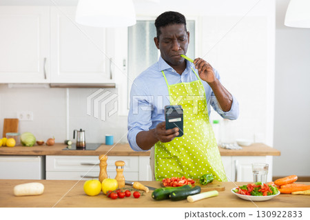 Man using smartphone while preparing food at home 130922833