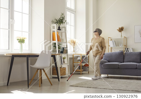 Senior elderly blind disabled woman in casual clothes with cane walking in the living room at home. 130922976