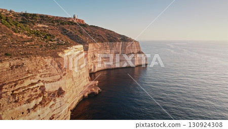 Malta: Golden sunset light reflecting on Dingli rocks cliffs, the highest point of Malta, with a radar dome on top and the Mediterranean Sea calm waters shining below, aerial drone flight 130924308
