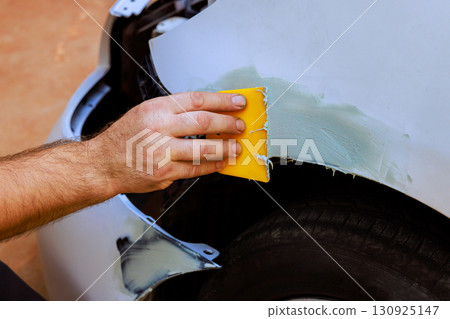 Car body repair process showing hand applying putty to damaged fender in garage setting 130925147