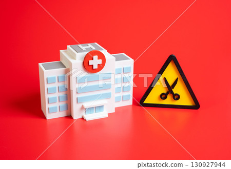 Hospital and the symbol of cuts. Cost reduction or dismissal of staff. Symbol of healthcare crisis, budget shortages, staff layoffs, medical closures, and public health decline. Hospital and the symbol of cuts. Cost reduction or dismissal of staff. Symbol of healthcare crisis, budget shortages, staff layoffs, medical closures, and public health decline. 130927944