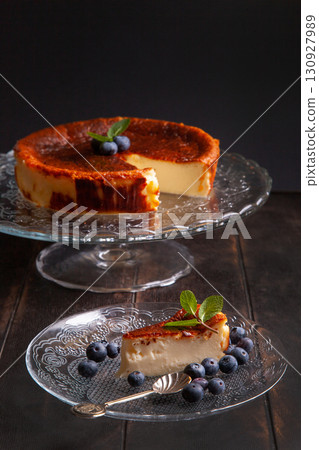 Homemade Basque burnt cheesecake with cream cheese, eggs and cream baked in a crumb crust. A slice of cheesecake on a plate with blueberries and mint leaves on dark background Homemade Basque burnt cheesecake with cream cheese, eggs and cream baked in a crumb crust. A slice of cheesecake on a plate with blueberries and mint leaves on dark background 130927989