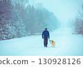 A man and his dog walk along a snowy road near a forest 130928126
