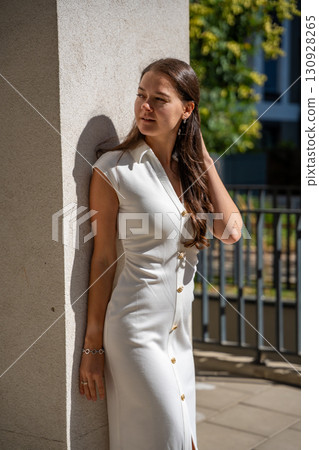 Young woman wearing a white midi dress walking outdoors in Old Money style. Concept of timeless fashion, graceful femininity and understated elegance in modern lifestyle. Young woman wearing a white midi dress walking outdoors in Old Money style. Concept of timeless fashion, graceful femininity and understated elegance in modern lifestyle. 130928265