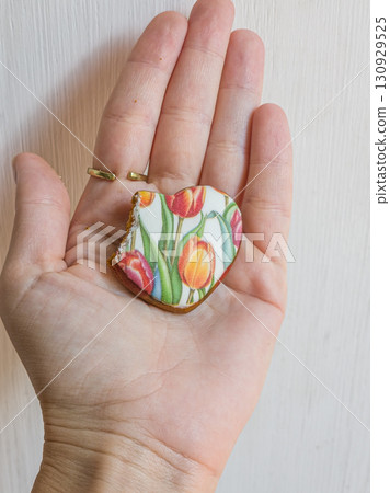 HumClose-up of a human hand holding a bitten heart-shaped gingerbread cookie. Sweet dessert and holiday treat concept.an hand holding gingerbread heart cookie. High quality photo 130929525