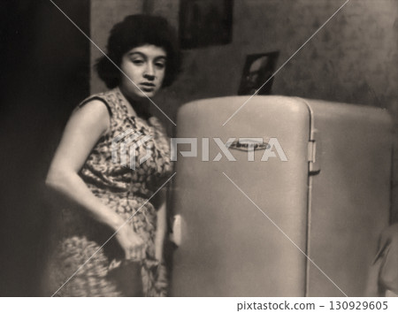 A vintage portrait of a beautiful young woman standing next to a newly purchased refrigerator. In the USSR, it was common to take photos with large new purchases. Retro photograph from 1961. A vintage portrait of a beautiful young woman standing next to a newly purchased refrigerator. In the USSR, it was common to take photos with large new purchases. Retro photograph from 1961. 130929605