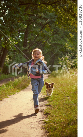 Girl running with dog on forest path in sunlight with laughter 130929736