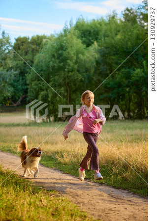 Girl running joyfully with dog along forest path in warm light 130929737